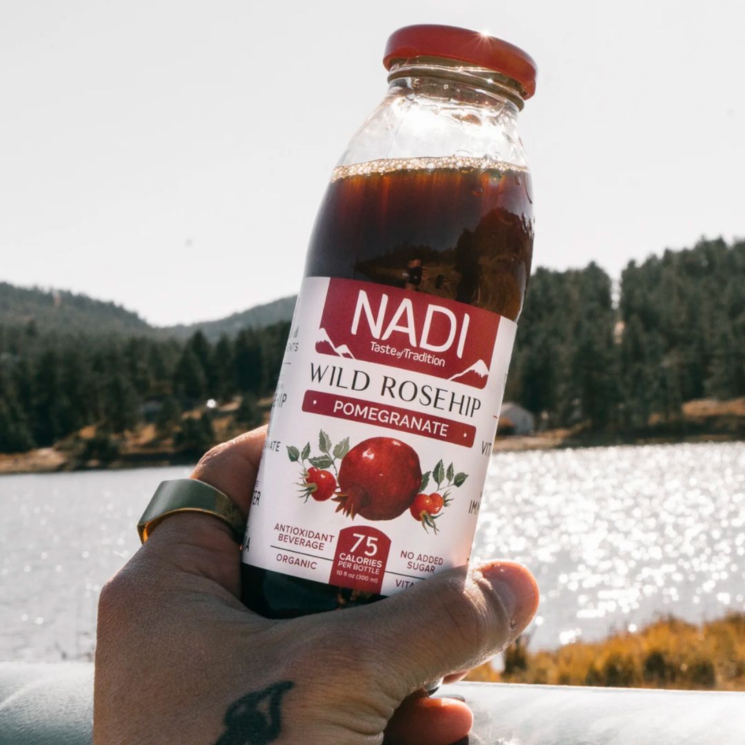 NADI Organic Rosehip Pomegranate Juice bottle held in front of lake 